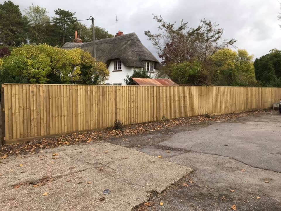 New closeboard fence along a lane, with a thatched cottage behind