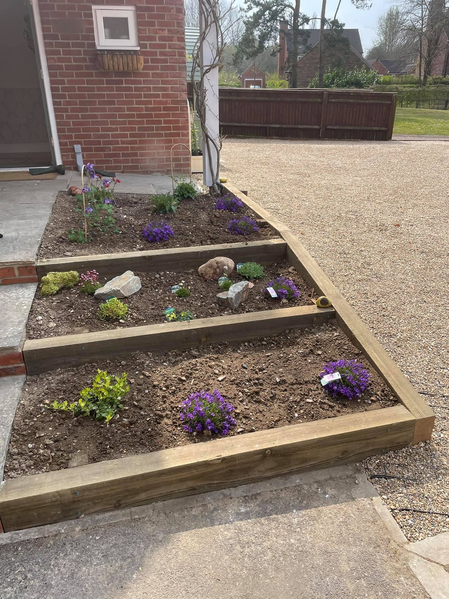 Tiered timber sleeper raised beds planted up beside a gravel drive