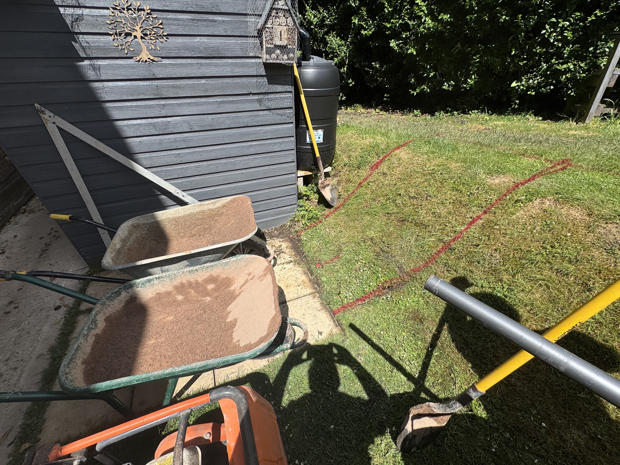 Work under way: wheelbarrows, tools and a new lawn edge marked out in paint beside a shed
