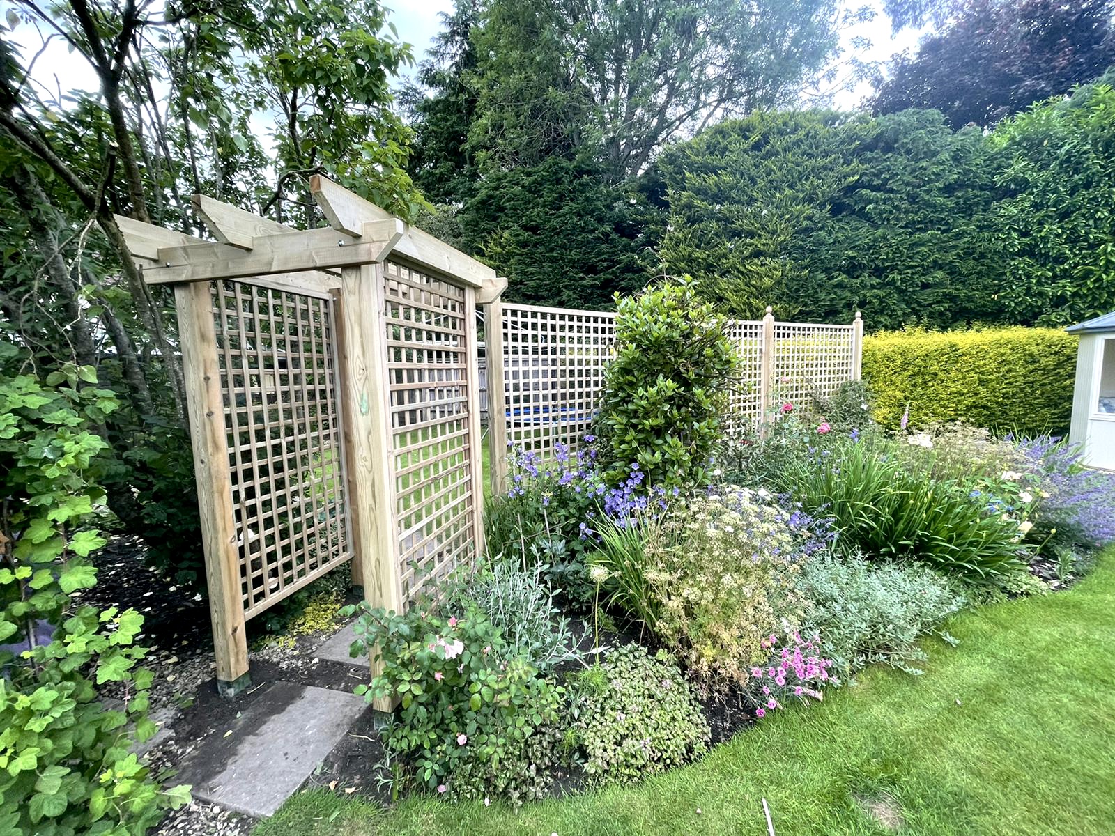 Timber pergola and trellis arch over a planted border