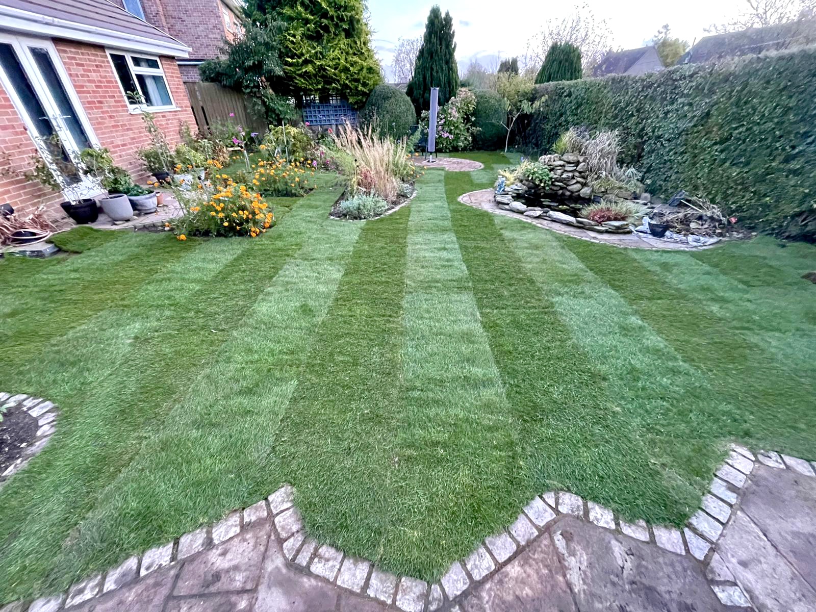 The same garden with a freshly laid striped lawn running up to the cobble-edged patio