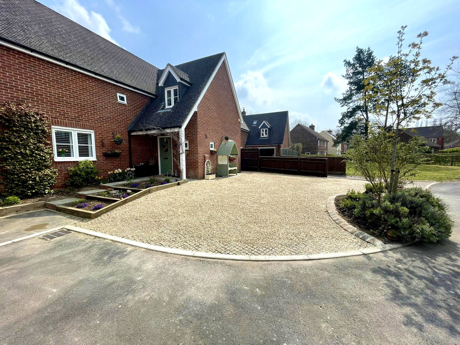 Gravel front driveway with cobble edging and raised planters in front of a brick house