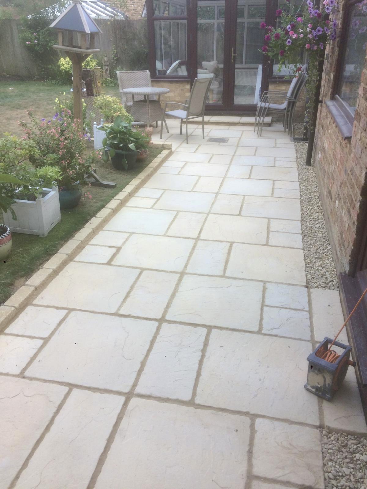 New pale sandstone patio laid beside a conservatory, edged with gravel