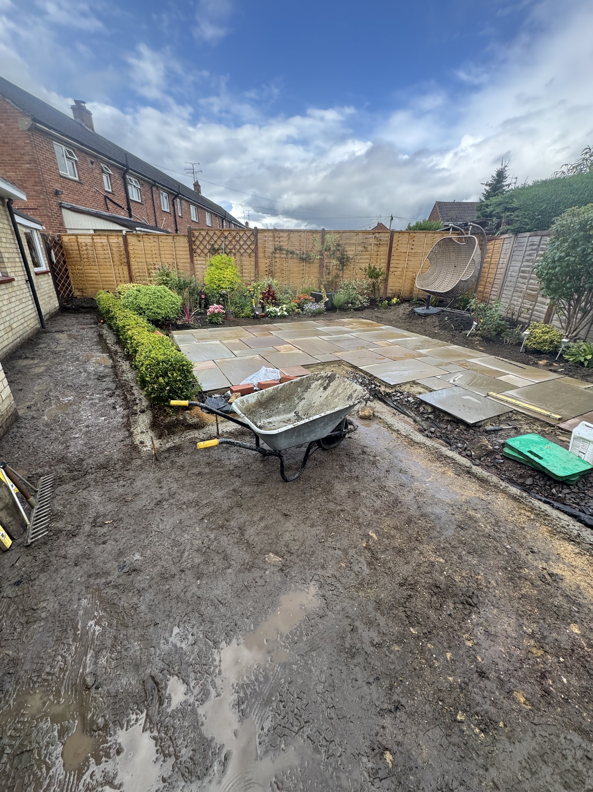 Rear garden mid-job, churned mud in front of a newly laid sandstone patio and box hedge