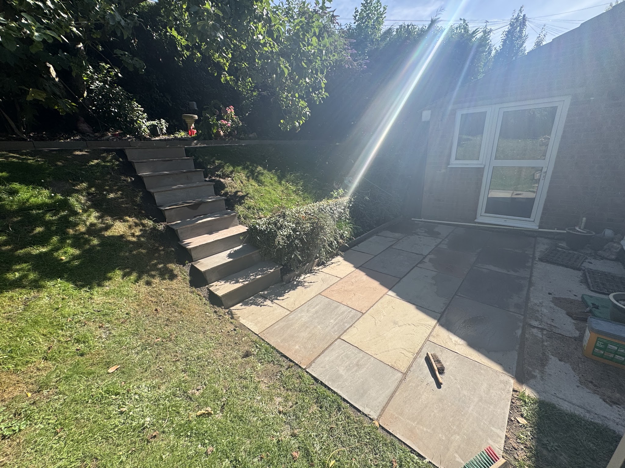 Timber steps built up a sloping lawn to a new Indian sandstone patio by a garden room
