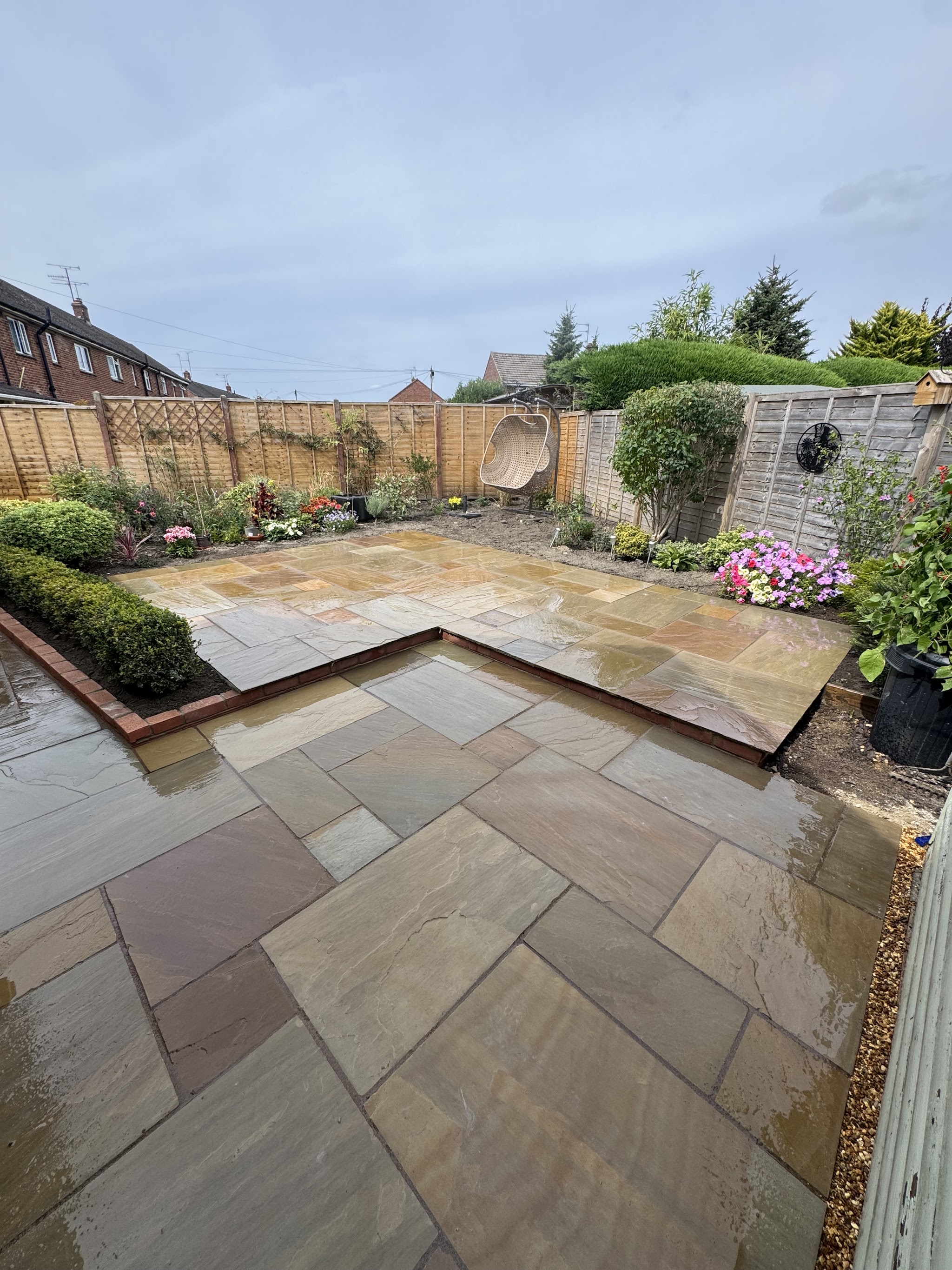 The finished Indian sandstone patio edged with low box hedging, wet after rain